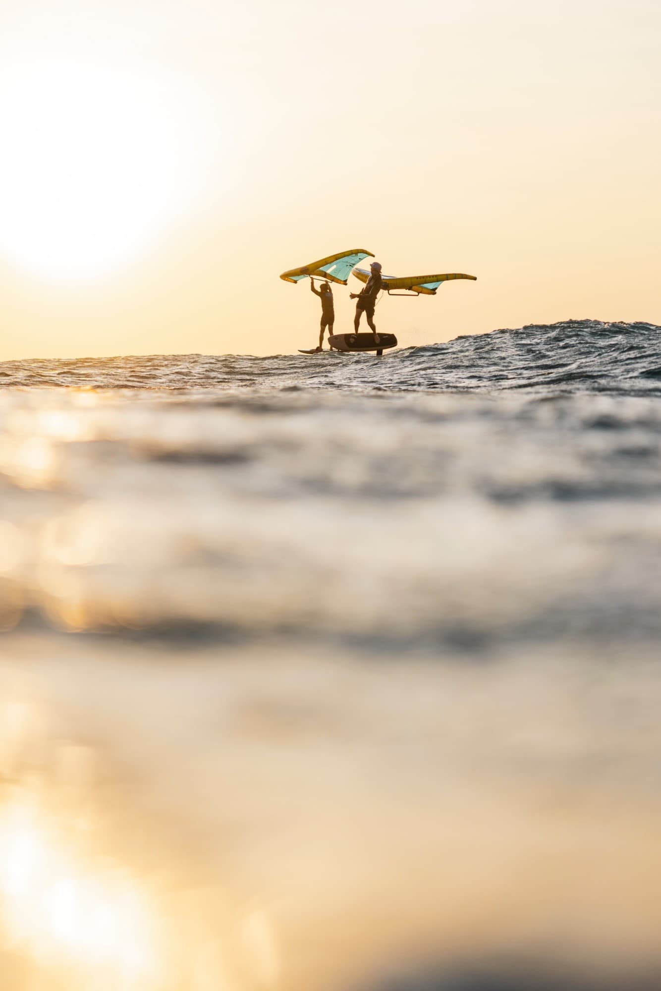 Two wing foilers lifting their wings at sunset in Brazil
