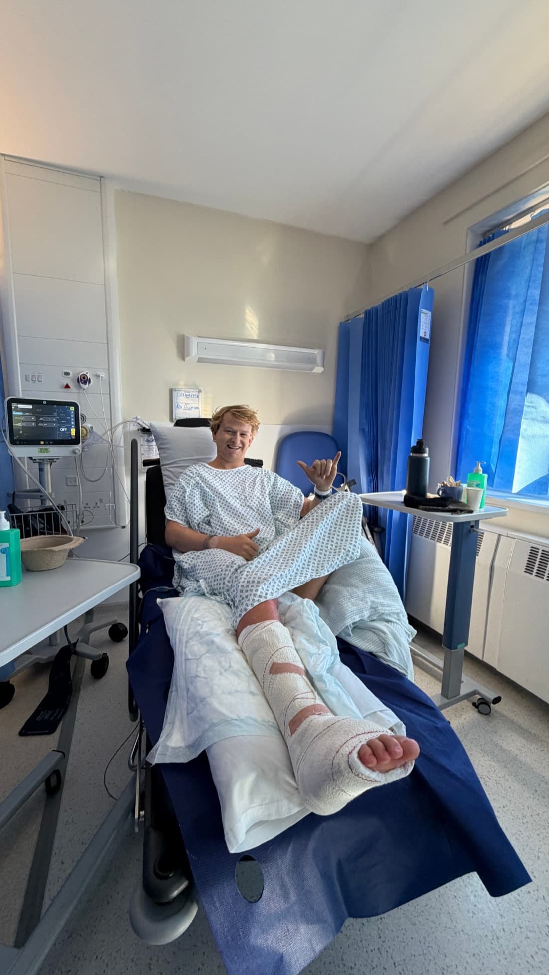 Toby in hospital after foot surgery, smiling and giving a shaka